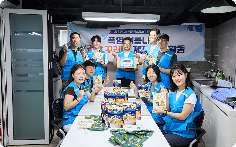 봉사자들이 삼계탕, 스프, 약과 등 알차게 구성된 후원 물품들을 들어 보이며 밝은 미소로 기념 촬영을 하고 있다.